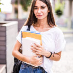 Young talented female student dressed in casual clothing walking around city . Attractive brunette woman enjoying free time